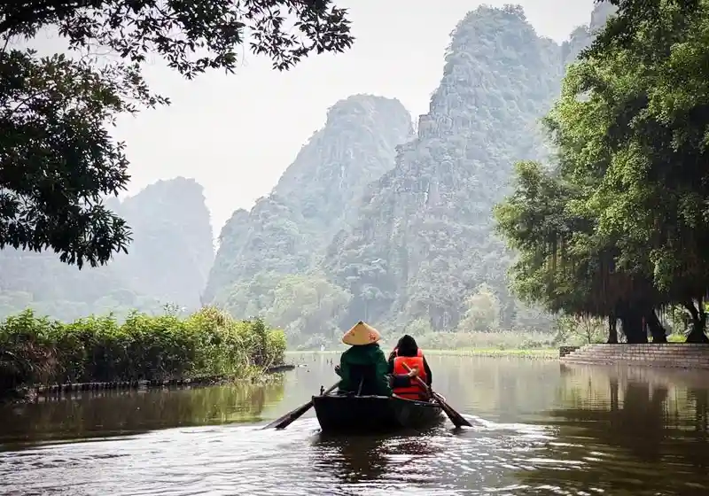 Boat rowing through Tam Coc river with limestone mountains in Ninh Binh